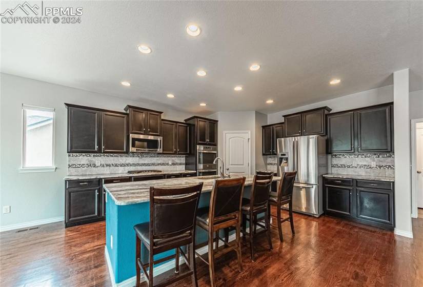 Kitchen with dark hardwood / wood-style flooring, an island with sink, backsplash, appliances with stainless steel finishes, and a breakfast bar area