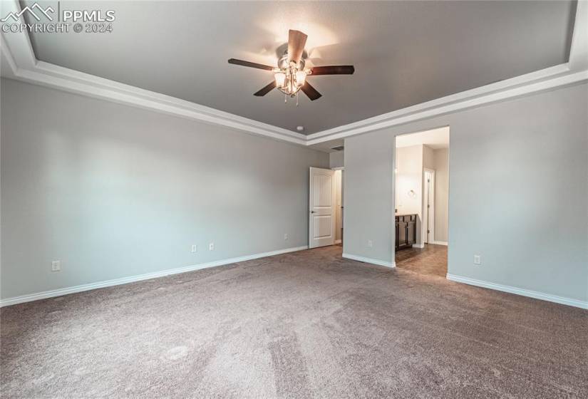 Unfurnished bedroom featuring a raised ceiling, ensuite bath, dark carpet, and ceiling fan