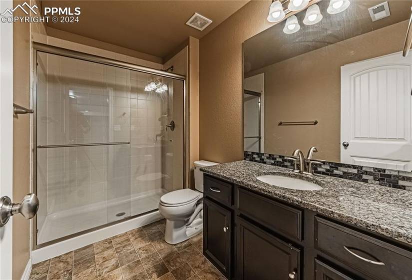 Bathroom featuring an enclosed shower, toilet, tile floors, backsplash, and large vanity