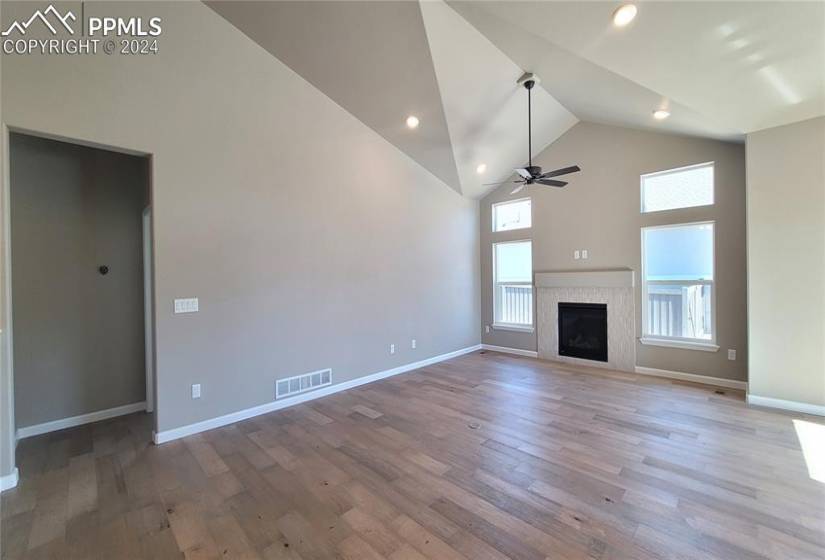 Great Room with vaulted ceilings, LED lighting, engineered wood flooring, floor outlet, ceiling fan, and a gas fireplace with beautiful tile surround!