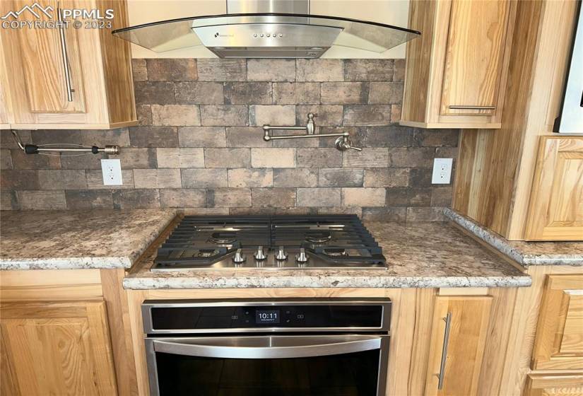 Gas cooktop with oven, pot filler, and stainless steel range hood