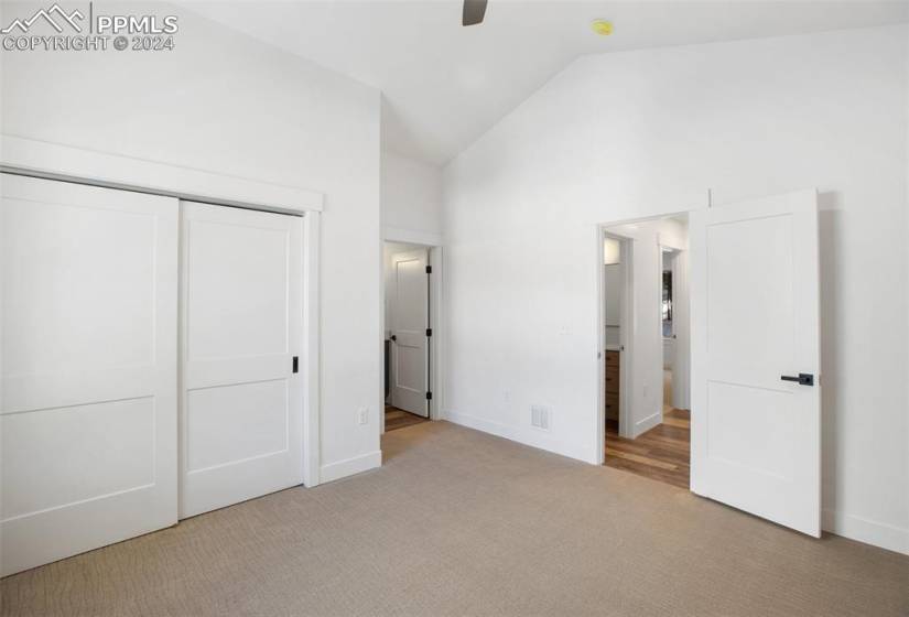 Unfurnished bedroom with a closet, ceiling fan, light colored carpet, and high vaulted ceiling