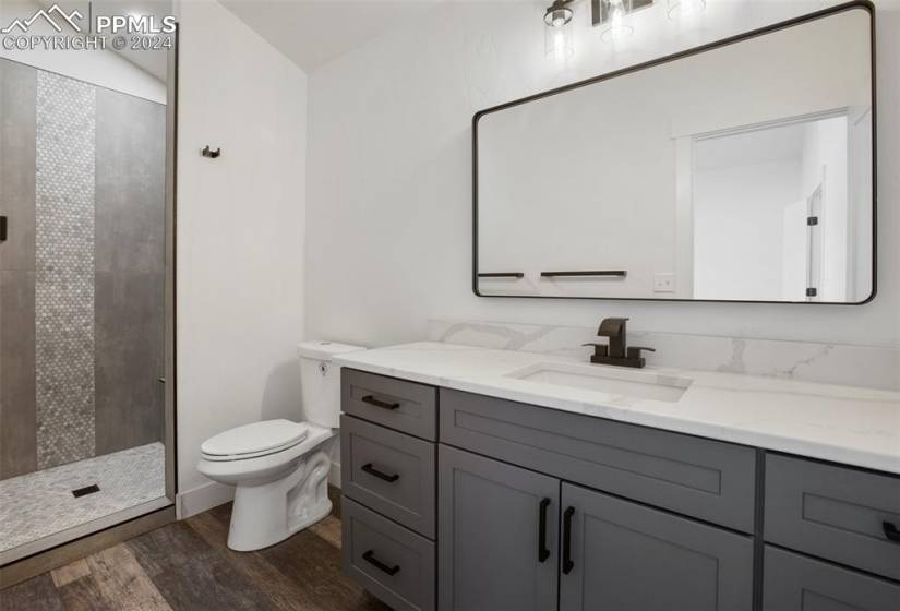 Bathroom with vanity, toilet, a tile shower, lofted ceiling, and wood-type flooring