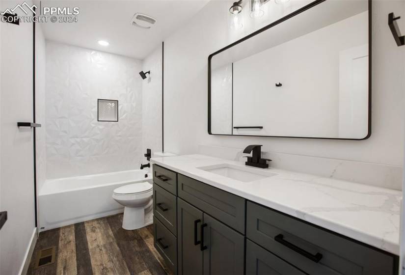 Full bathroom featuring wood-type flooring, toilet, tiled shower / bath, and vanity with extensive cabinet space