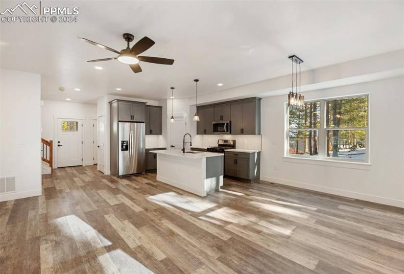 Kitchen featuring pendant lighting, ceiling fan with notable chandelier, appliances with stainless steel finishes, light hardwood / wood-style floors, and an island with sink