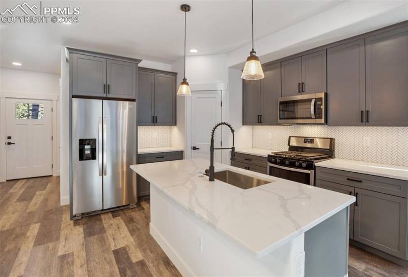 Kitchen featuring a center island with sink, light stone countertops, decorative light fixtures, and stainless steel appliances