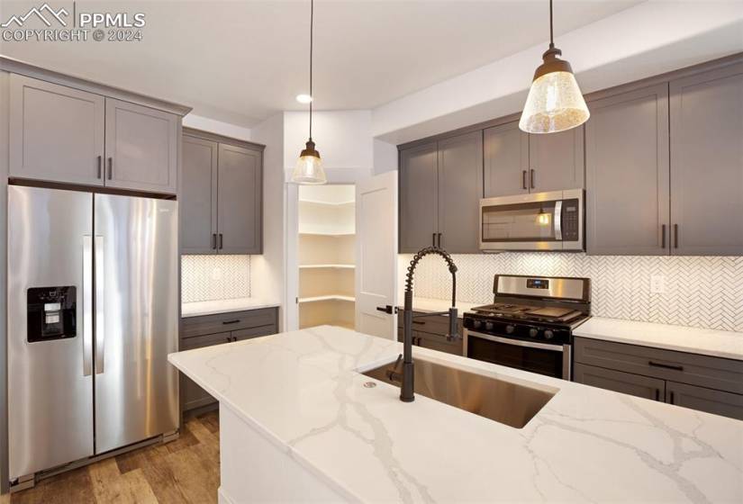 Kitchen featuring appliances with stainless steel finishes, light stone countertops, backsplash, and decorative light fixtures