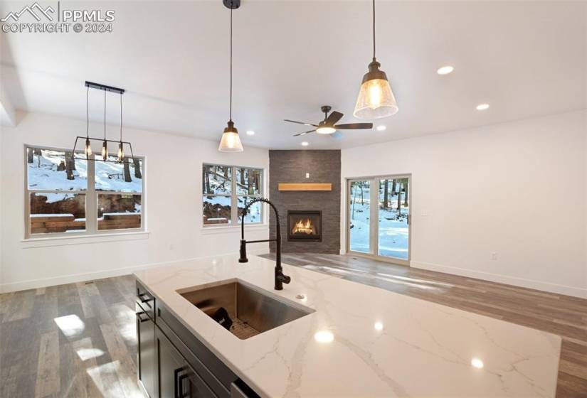 Kitchen with pendant lighting, light stone countertops, light hardwood / wood-style floors, and a fireplace