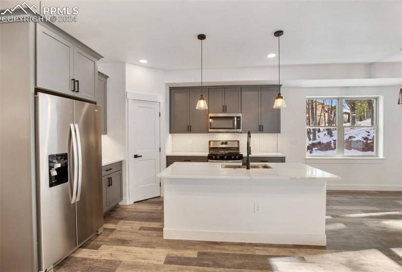 Kitchen featuring gray cabinetry, hanging light fixtures, stainless steel appliances, and light stone counters