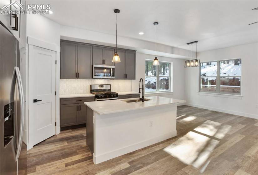 Kitchen featuring light hardwood / wood-style flooring, a center island with sink, tasteful backsplash, decorative light fixtures, and appliances with stainless steel finishes