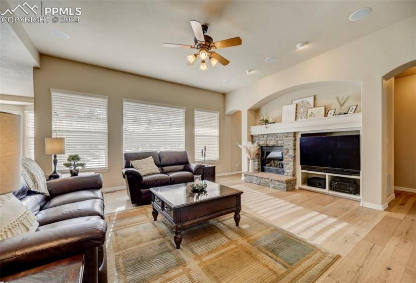 Living room with a stone fireplace, light hardwood / wood-style flooring, ceiling fan, and built in features