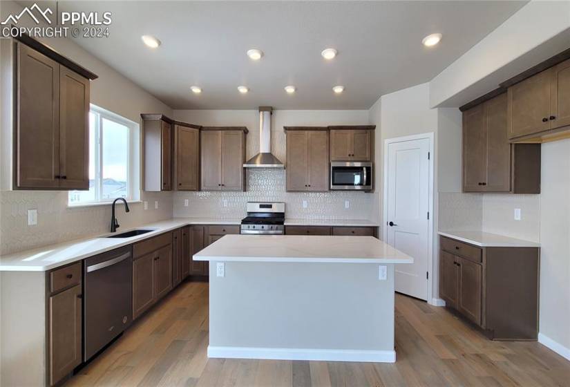Kitchen with quartz countertops, pantry, large island providing additional seating, and stainless steel pyramid hood, gas range, microwave, dishwasher, and single bowl composite sink!