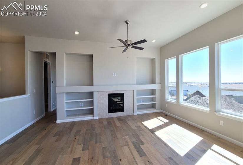 Great room with engineered wood flooring, floor outlet, ceiling fan, LED lighting, gas fireplace with beautiful tile surround, and a built-in entertainment center!