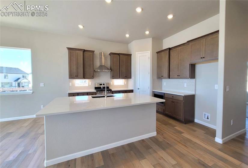 Kitchen with quartz countertops, pantry, large island providing additional seating, and stainless steel gas range, pyramid hood, microwave, and dishwasher!