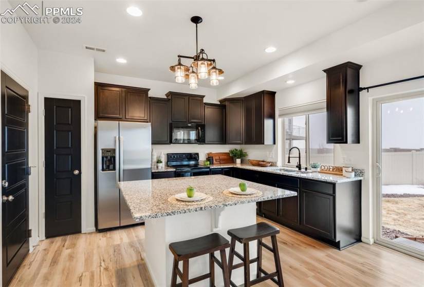 Kitchen with an inviting chandelier, light hardwood / wood-style flooring, a kitchen island, and black appliances
