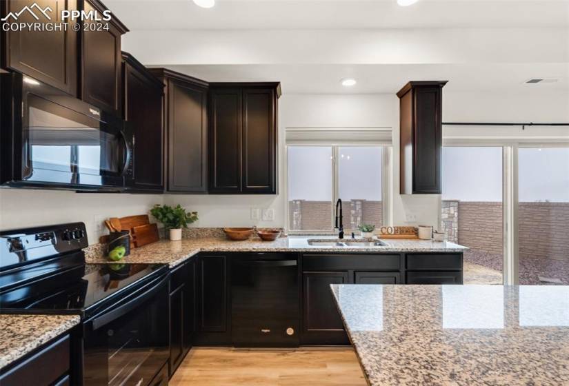 Kitchen featuring plenty of natural light, light hardwood / wood-style floors, light stone counters, and black appliances