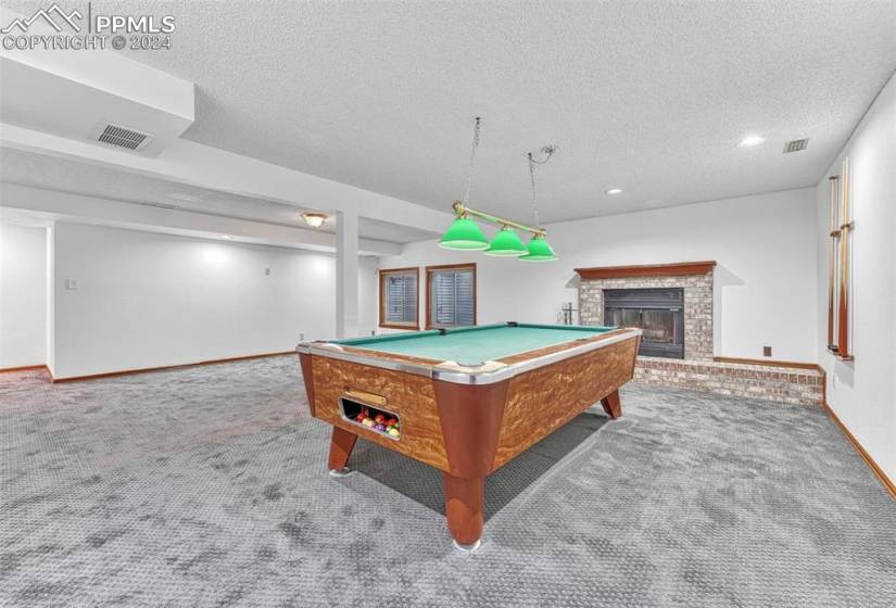 The Basement Recreation Room is a great place to have fun and entertain with a pool table, pendant lights, and a wood fireplace with brick surround, raised hearth, and mantle.