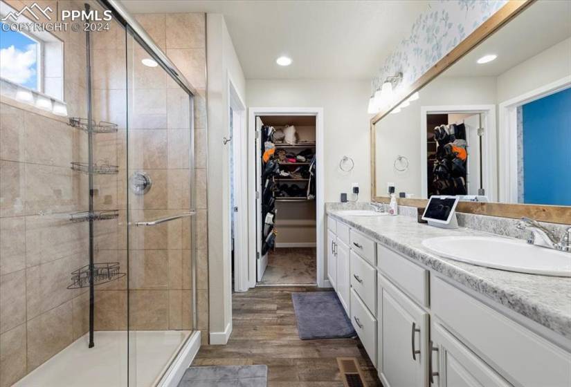 Luxurious Primary Shower Bathroom with dual sink vanity, framed mirror, walk in closet, and enclosed tiled shower