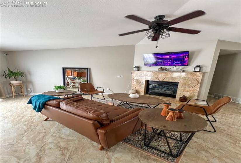 Living room with ceiling fan, light tile floors, a tile fireplace, and a textured ceiling