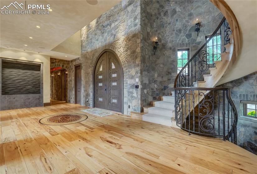 The entryway makes a statement with stunning arched wood doors, stone, wood mosaic inlay, dramatic spiral staircase, water feature