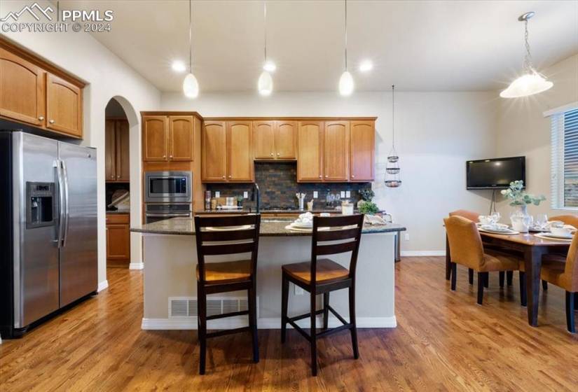 The Kitchen features a pantry, counter bar with pendant lights, wood cabinets and island with granite countertops.