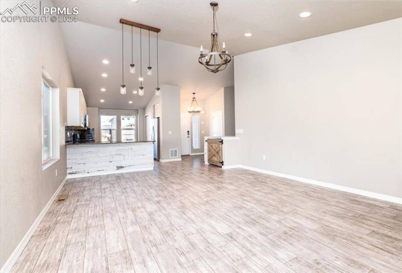 Living/family room with light hardwood / wood-style floors, high vaulted ceiling, and an inviting chandelier