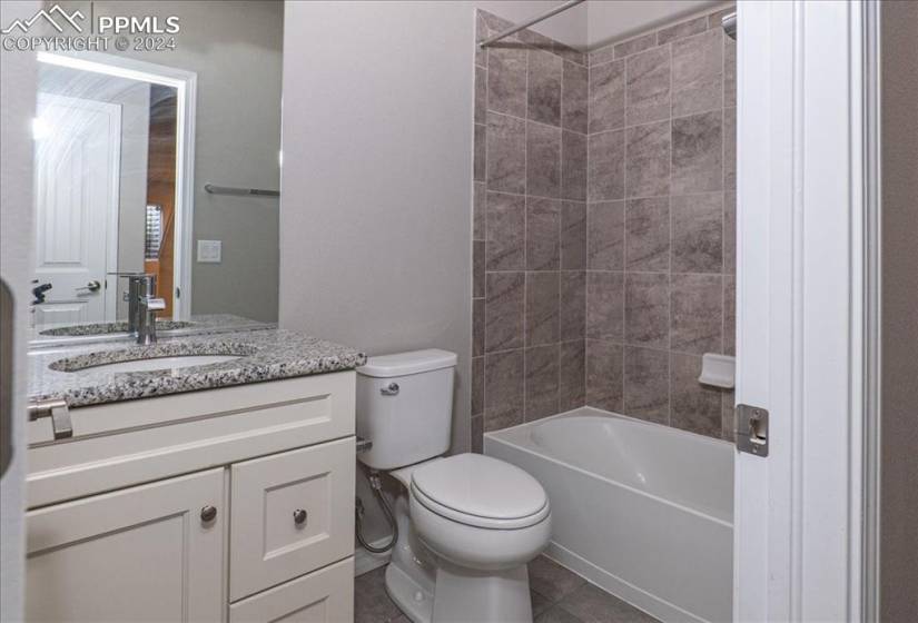 Downstairs full bathroom featuring tile flooring, large vanity, toilet, and tiled shower / bath