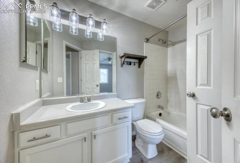 Full upper level bathroom featuring a textured ceiling, vanity, tiled shower / bath, and toilet with access through the hallway and Primary Bedroom