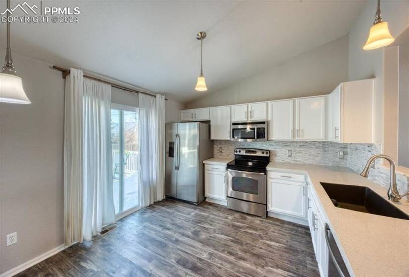 Walk Out Kitchen with pendant lights, white cabinets with ample counterspace for easy food prep, and stainless steel appliances that stay.