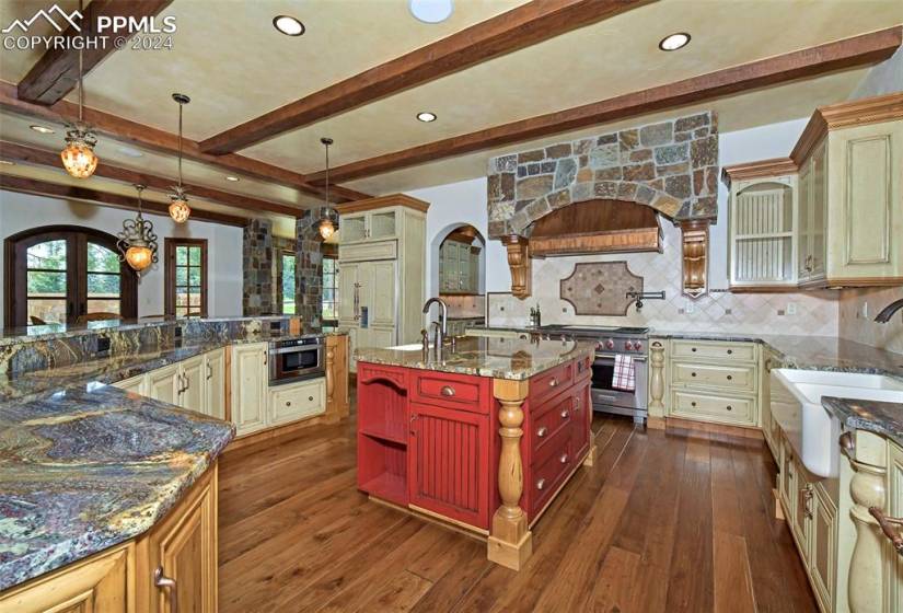 Kitchen featuring high end appliances, backsplash, a kitchen island with sink, dark hardwood / wood-style floors, and dark stone countertops