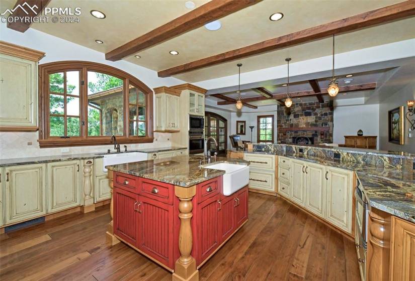 Kitchen with a center island with sink, cream cabinets, backsplash, ceiling fan, and a stone fireplace