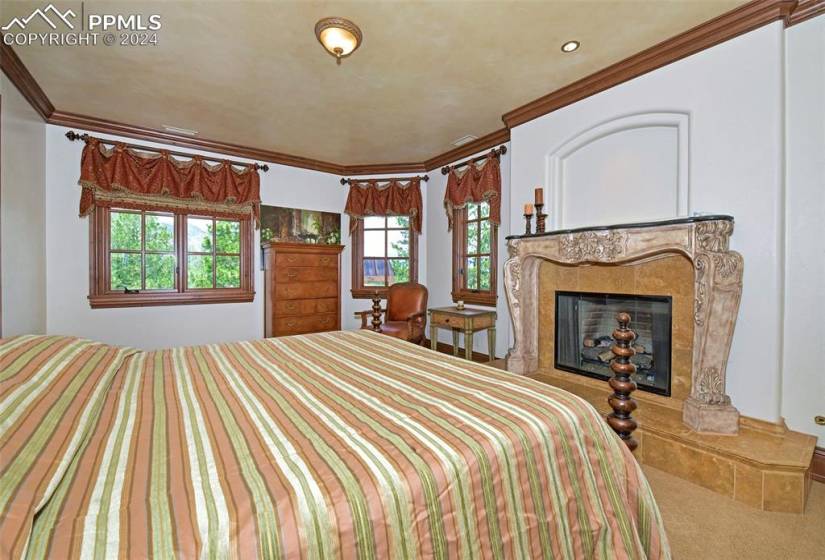 Carpeted bedroom with a fireplace and crown molding