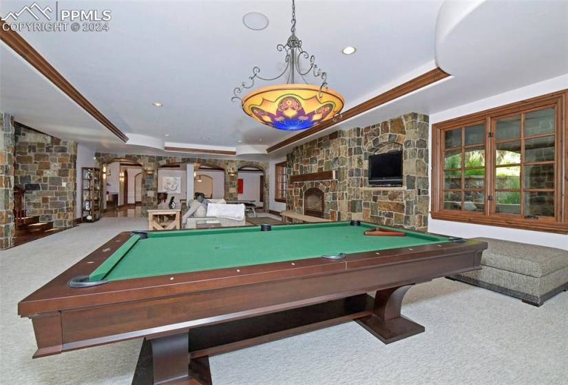 Rec room with a raised ceiling, carpet floors, billiards, a stone fireplace, and decorative columns