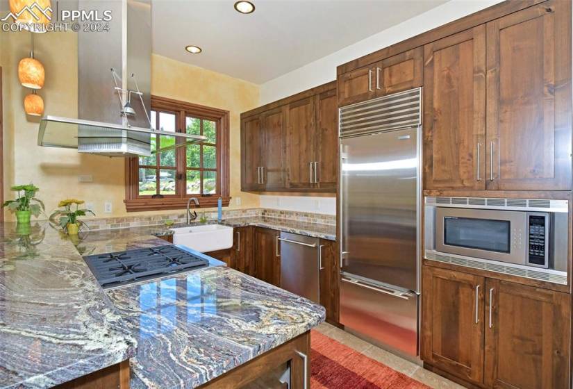 Kitchen featuring built in appliances, pendant lighting, light stone countertops, sink, and light tile floors