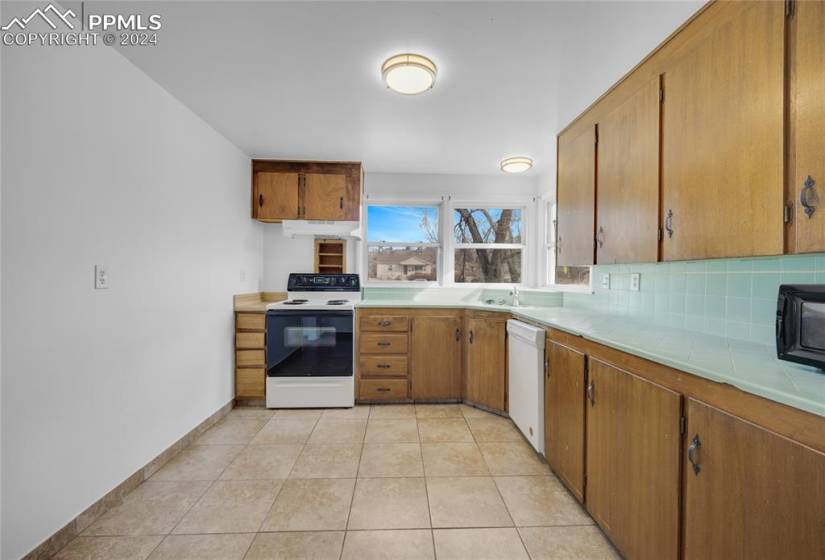 Kitchen with white appliances, light tile floors, backsplash, and sink