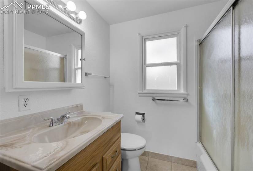 Full bathroom with bath / shower combo with glass door, large vanity, tile floors, and toilet