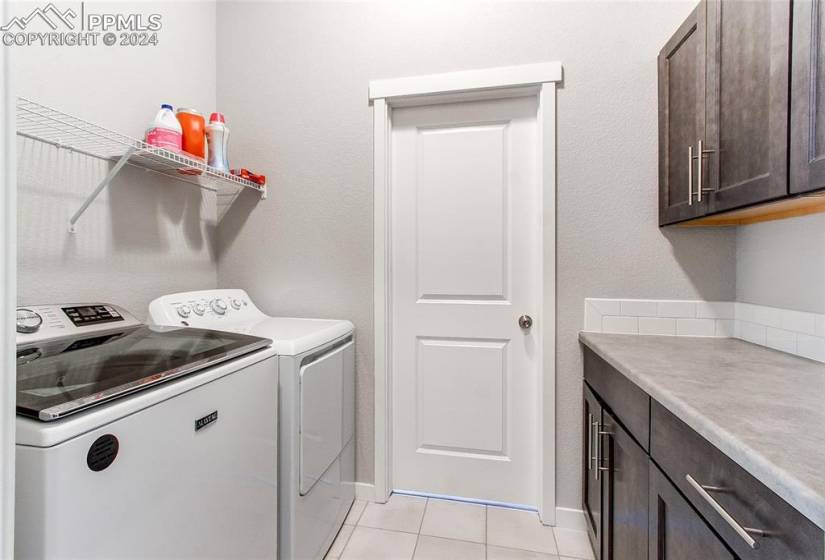 Washroom featuring light tile floors, washing machine and dryer, and cabinets