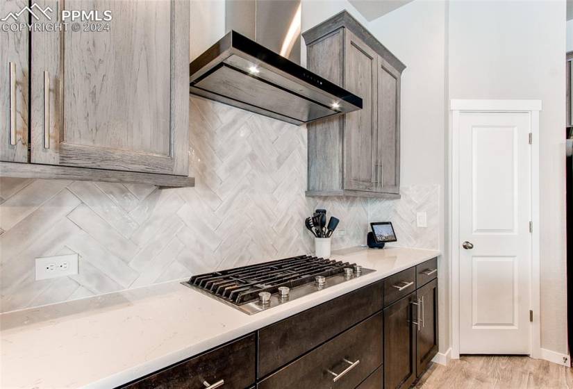 Kitchen with stainless steel gas stovetop, dark brown cabinetry, tasteful backsplash, light hardwood / wood-style flooring, and wall chimney range hood