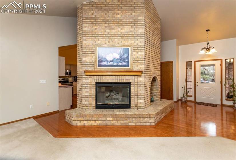 Unfurnished living room with a fireplace, brick wall, an inviting chandelier, and wood-type flooring.