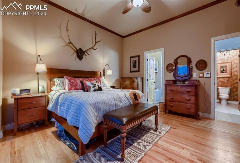 Bedroom with light hardwood / wood-style floors, crown molding, ceiling fan, and ensuite bathroom
