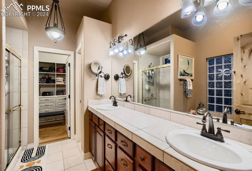 Primary bathroom with double sink vanity, tile flooring, walk in shower and large walk in closet