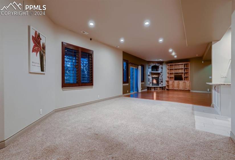Walkout basement family room featuring light colored carpet, built ins, a wet bar area, and third stone fireplace