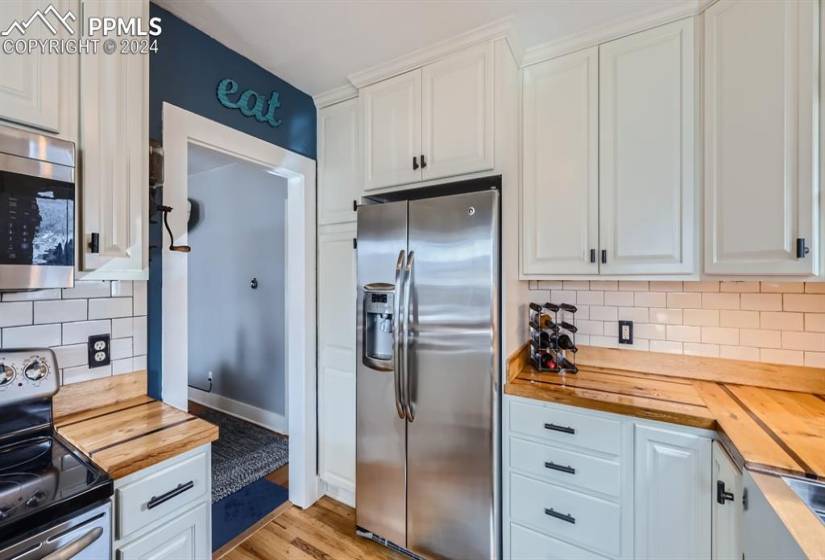 Kitchen - stainless steal appliances, light hardwood wood-style floors, tile backsplash, and white cabinets with new handles