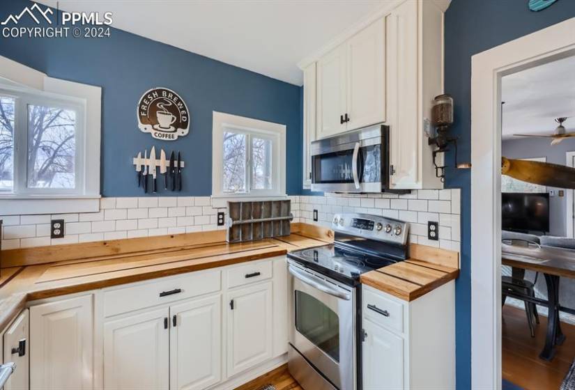 Kitchen - stainless steal appliances, light hardwood wood-style floors, tile backsplash, and white cabinets with new handles, and a healthy amount of sunlight