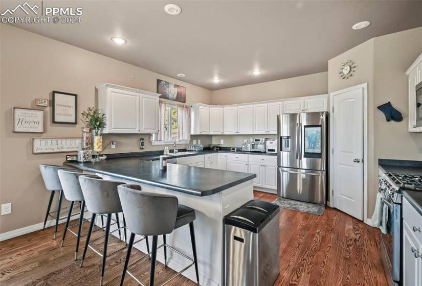 Kitchen with dark hardwood / wood-style floors, appliances with stainless steel finishes, a breakfast bar, and kitchen peninsula
