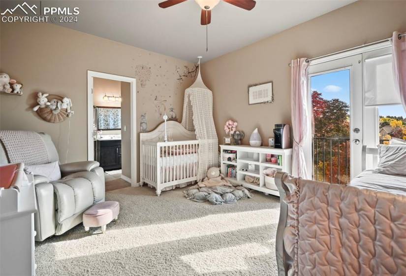 Carpeted bedroom featuring ceiling fan, a crib, ensuite bathroom, and access to exterior