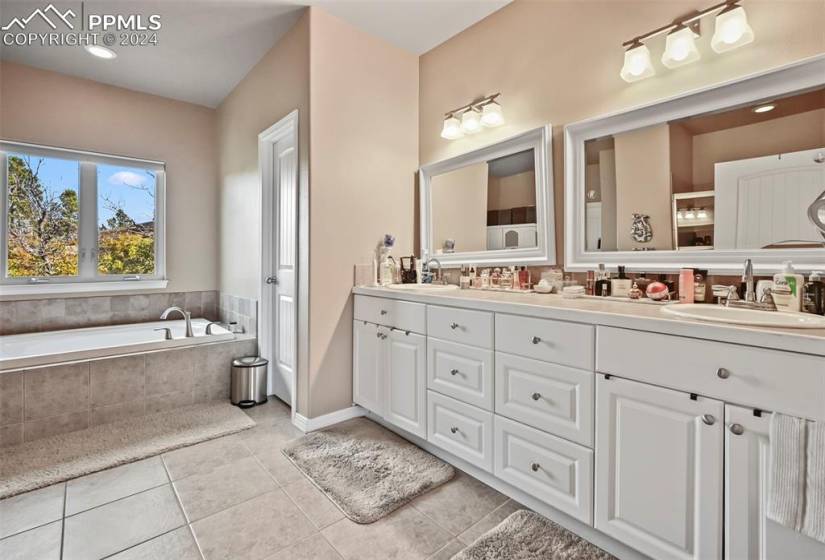 Bathroom featuring a relaxing tiled bath, double sink, tile floors, and oversized vanity