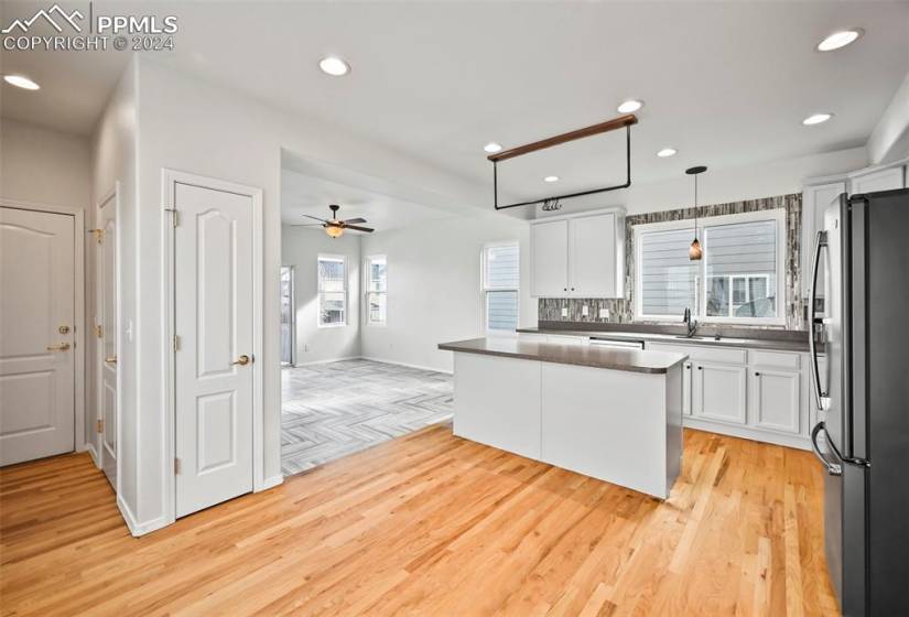 Kitchen with pendant lighting, light wood-type flooring, white cabinetry, stainless steel refrigerator with ice dispenser, and ceiling fan