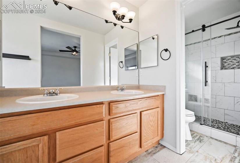 Bathroom featuring ceiling fan, a shower with door, dual vanity, toilet, and tile floors