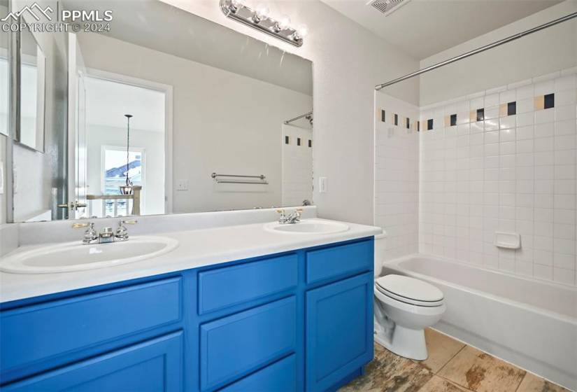 Full bathroom with dual sinks, tiled shower / bath combo, oversized vanity, toilet, and tile floors